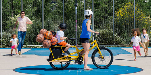 Viele Kinder laufen auf ein Yuba Kombi Longtail Lastenrad zu